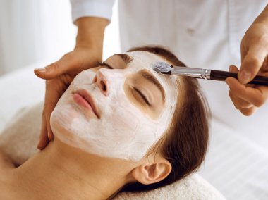 Güzel esmer kadın kapalı gözlerle kozmetik maske takmaktan zevk alıyor. Tıp ve kaplıca merkezi kavramlarında rahatlatıcı tedavi