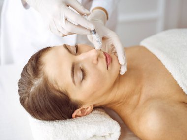 Güzellik uzmanı, genç esmer kadının yüzüne şırıngayla güzellik prosedürü uyguluyor. Kozmetik ilaç ve ameliyat, güzellik iğneleri.