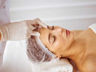 Güzellik uzmanı, genç esmer kadının yüzüne şırıngayla güzellik prosedürü uyguluyor. Kozmetik ilaç ve ameliyat, güzellik iğneleri.