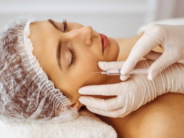 Güzellik uzmanı, genç esmer kadının yüzüne şırıngayla güzellik prosedürü uyguluyor. Kozmetik ilaç ve ameliyat, güzellik iğneleri.