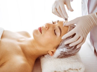 Güzellik uzmanı, genç esmer kadının yüzüne şırıngayla güzellik prosedürü uyguluyor. Kozmetik ilaç ve ameliyat, güzellik iğneleri.