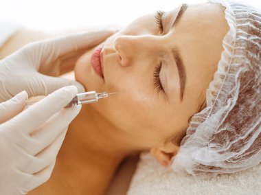 Güzellik uzmanı, genç esmer kadının yüzüne şırıngayla güzellik prosedürü uyguluyor. Kozmetik ilaç ve ameliyat, güzellik iğneleri.