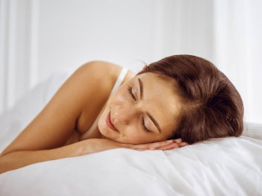 Güzel, genç, esmer kadın yatakta rahat ve mutlu bir şekilde yatarken uyuyor. Günaydın konsept.