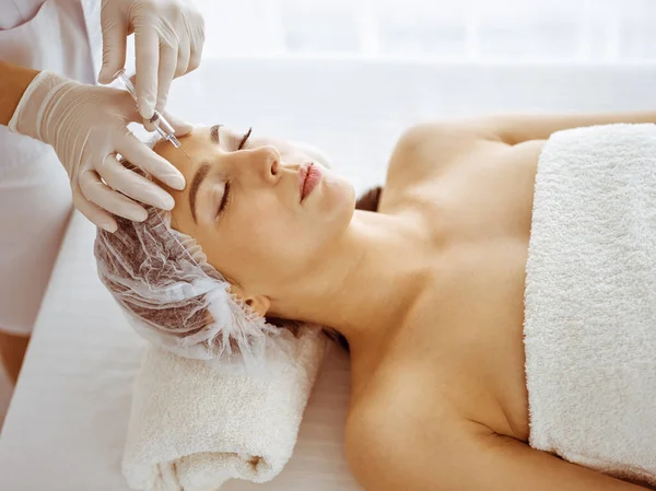 Beautician doing beauty procedure with syringe to face of young brunette woman. Cosmetic medicine and surgery, beauty injections