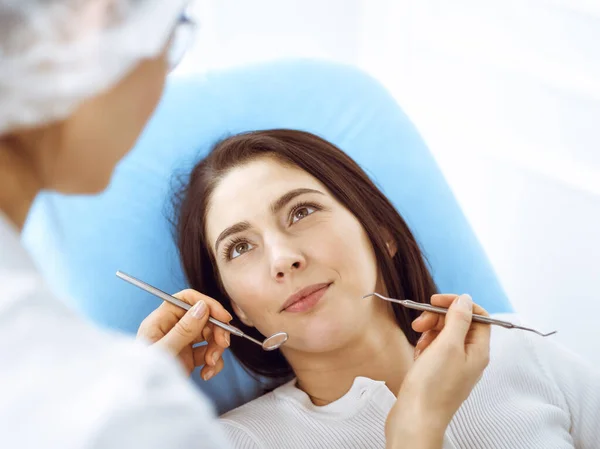 Lachende brunette vrouw wordt onderzocht door tandarts in de tandheelkundige kliniek. Handen van een arts met tandheelkundige instrumenten in de buurt van de mond van patiënten. Gezonde tanden en geneeskundeconcept — Stockfoto