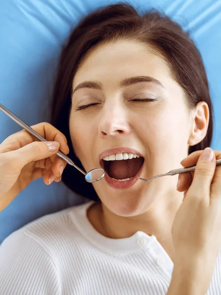 在牙科诊所接受牙医检查的面带微笑的黑发女人。医生手拿着牙科器械靠近病人的嘴。健康的牙齿和医学概念 — 图库照片