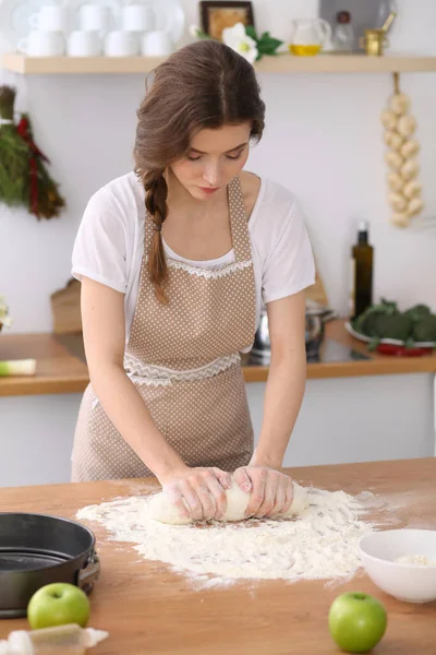 Jonge brunette vrouw koken pizza of handgemaakte pasta in de keuken. Huisvrouw maakt deeg op houten tafel. Dieet-, voedings- en gezondheidsconcept — Stockfoto