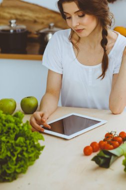 Genç bir kadın mutfakta yemek pişirmek için yeni bir tarif arıyor. Ev hanımı tablet bilgisayar ve kredi kartıyla online alışveriş yapıyor.