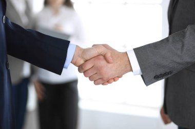 İş adamları toplantıdan ya da pazarlıktan sonra iş arkadaşlarıyla el sıkışıyorlar. Yakın plan. Modern ofisteki bir grup tanınmamış iş adamı ve kadın. Takım çalışması, ortaklık ve tokalaşma
