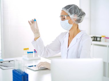 Koruyucu gözlüklü profesyonel kadın bilim adamı laboratuarda reaktörlerle araştırma tüpü kullanıyor. Tıp ve araştırma kavramları