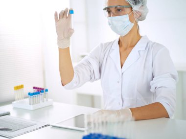 Koruyucu gözlüklü profesyonel kadın bilim adamı laboratuarda reaktörlerle araştırma tüpü kullanıyor. Tıp ve araştırma kavramları