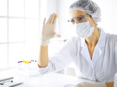 Koruyucu gözlüklü profesyonel kadın bilim adamı laboratuarda reaktörlerle araştırma tüpü kullanıyor. Tıp ve araştırma kavramları