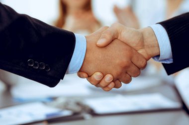 İş arkadaşları alkışlayıp alkışlarken iş adamları toplantıda tokalaşıyor. Modern beyaz ofisteki bir grup tanınmayan iş adamı ve kadın. Başarı takım çalışması, ortaklık ve tokalaşma