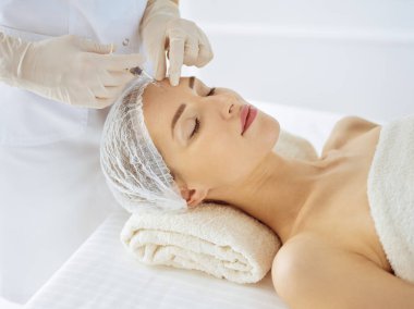 Güzel bir kadın kapalı gözlerle güzellik iğneleri yaptırıyor. Güzellik uzmanı elleri şırıngayla kadın yüzüne güzellik prosedürü uyguluyor. Kozmetik tıp ve cerrahi konsepti