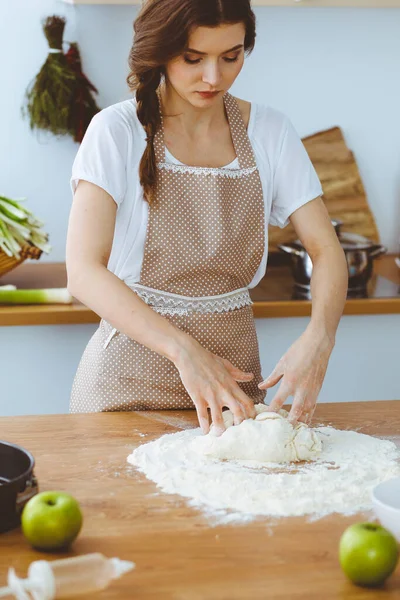젊은 갈색 머리 여자가 피자나 손으로 만든 파스타를 주방에서 요리하고 있습니다. 주부는 나무 식탁에서 반죽을 준비 한다. 식사, 음식 및 건강에 대한 개념 — 스톡 사진