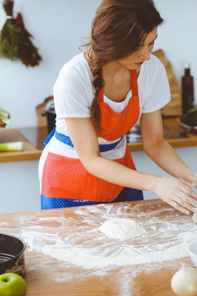 Jovem morena cozinhando pizza ou massa artesanal na cozinha. Dona de casa que prepara a massa de farinha na mesa de madeira. Conceito de alimentação, alimentação e saúde — Fotografia de Stock