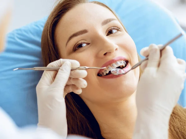 Uśmiechnięta młoda kobieta z nawiasami ortodontycznymi badana przez dentystę w klinice dentystycznej. Zdrowe zęby i koncepcja medycyny — Zdjęcie stockowe