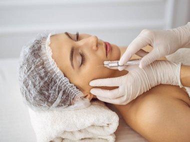 Güzellik uzmanı, genç esmer kadının yüzüne şırıngayla güzellik prosedürü uyguluyor. Kozmetik ilaç ve ameliyat, güzellik iğneleri.