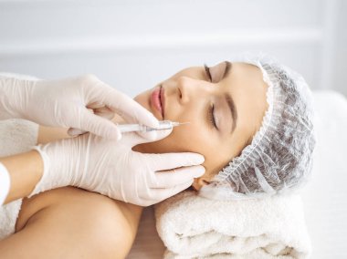 Güzellik uzmanı, genç esmer kadının yüzüne şırıngayla güzellik prosedürü uyguluyor. Kozmetik ilaç ve ameliyat, güzellik iğneleri.