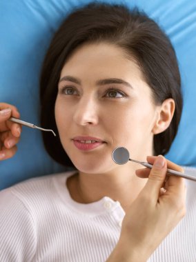 Gülümseyen esmer kadın diş hekimi tarafından muayene ediliyor. Hastanın ağzının yanında diş aletleri tutan bir doktorun elleri. Sağlıklı diş ve ilaç konsepti