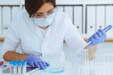 Koruyucu gözlüklü profesyonel kadın bilim adamının laboratuarda reaktörlerle deney yapması. Tıp ve araştırma konsepti