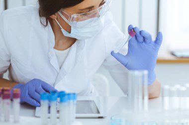 Koruyucu gözlüklü profesyonel kadın bilim adamının laboratuarda reaktörlerle deney yapması. Tıp ve araştırma konsepti