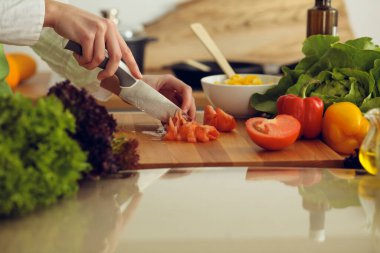 Mutfakta pişen bilinmeyen insan elleri. Kırmızı domatesleri dilimleyen kadın. Sağlıklı yemek ve vejetaryen gıda konsepti.