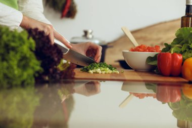 Mutfakta pişen bilinmeyen insan elleri. Yeşil soğan dilimleyen bir kadın. Sağlıklı yemek ve vejetaryen gıda konsepti.