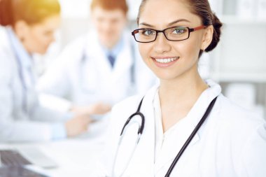 Mutlu gülümseyen kadın doktor tıbbi personelle toplantıda oturup kameraya bakıyor. Tıp konsepti