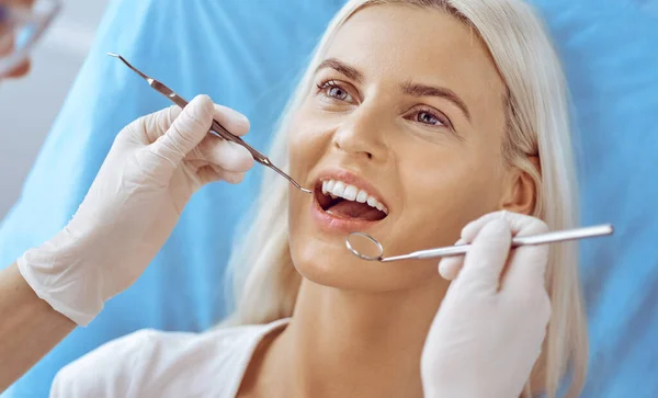 Leende blond kvinna undersökt av tandläkare på tandvårdskliniken. Friska tänder och medicin koncept — Stockfoto