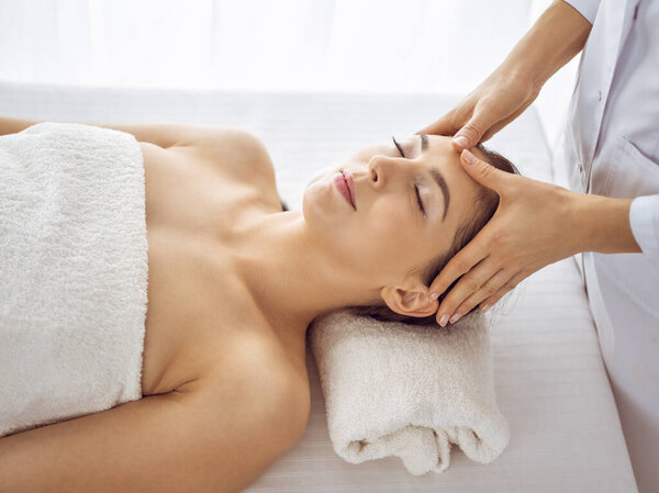 Beautiful brunette woman enjoying facial massage with closed eyes. Relaxing treatment in medicine and spa center concepts