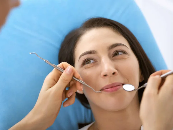 Lachende brunette vrouw wordt onderzocht door tandarts in de tandheelkundige kliniek. Handen van een arts met tandheelkundige instrumenten in de buurt van de mond van patiënten. Gezonde tanden en geneeskundeconcept — Stockfoto