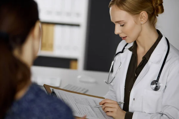 Vrolijke glimlachende vrouwelijke arts en geduldige vrouw bespreken het huidige gezondheidsonderzoek tijdens het zitten in de kliniek. Perfecte medische dienst in het ziekenhuis. Geneesmiddelenconcept — Stockfoto