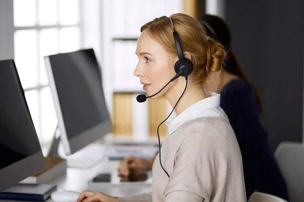 Femme d'affaires parlant par casque pendant qu'elle était assise au bureau. Centre d'appels et divers groupes de personnes en affaires — Photo