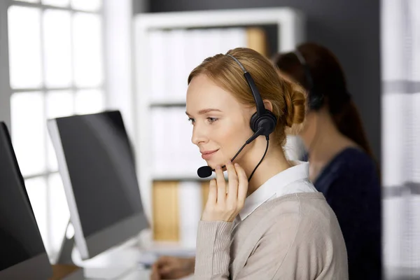 Femme d'affaires parlant par casque pendant qu'elle était assise au bureau. Centre d'appels et divers groupes de personnes en affaires — Photo