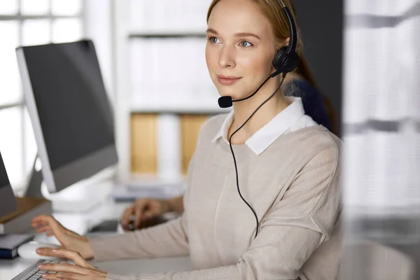 Femme d'affaires parlant par casque pendant qu'elle était assise au bureau. Centre d'appels et divers groupes de personnes en affaires — Photo