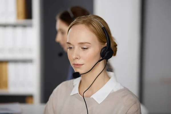 Femme d'affaires parlant par casque pendant qu'elle était assise au bureau. Centre d'appels et divers groupes de personnes en affaires — Photo