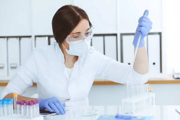 Close-up de cientista profissional feminino em óculos de proteção fazendo experiência com reagentes em laboratório. Medicina e conceito de pesquisa — Fotografia de Stock