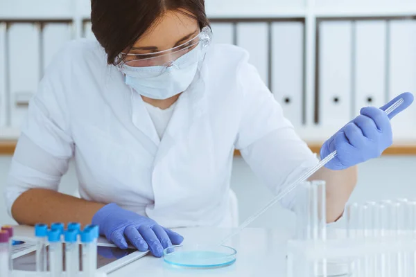 Close-up de cientista profissional feminino em óculos de proteção fazendo experiência com reagentes em laboratório. Medicina e conceito de pesquisa — Fotografia de Stock