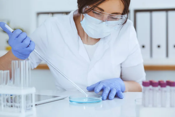 Close-up de cientista profissional feminino em óculos de proteção fazendo experiência com reagentes em laboratório. Medicina e conceito de pesquisa — Fotografia de Stock