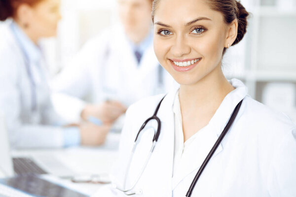 Happy smiling woman-doctor sitting and looking at camera at meeting with medical staff . Medicine concept