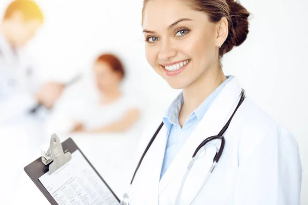 Vrolijke lachende vrouw-dokter op de achtergrond van zijn patiënt in het bed. Geneesmiddelenconcept — Stockfoto