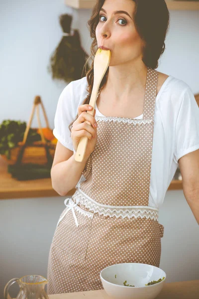 Jonge brunette die kookt in de keuken. Huisvrouw met een houten lepel in haar hand. Voedsel- en gezondheidsconcept — Stockfoto