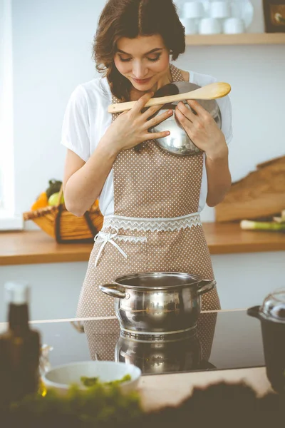 Jovem morena cozinhando sopa na cozinha. Dona de casa segurando colher de madeira na mão. Conceito de alimentação e saúde — Fotografia de Stock