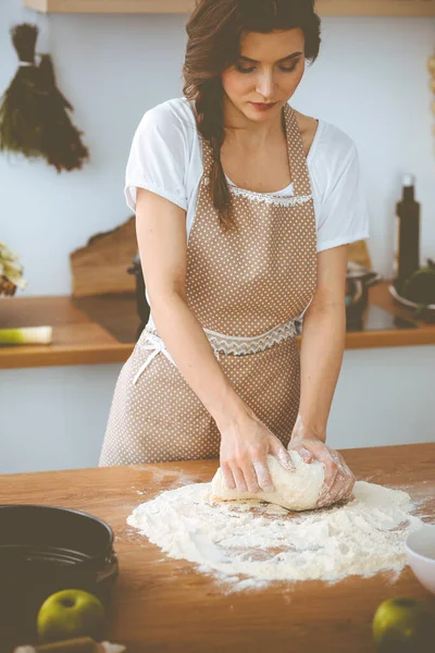 Młoda brunetka gotuje pizzę lub ręcznie robiony makaron w kuchni. Gospodyni domowa przygotowuje ciasto na drewnianym stole. Koncepcja diety, żywności i zdrowia — Zdjęcie stockowe