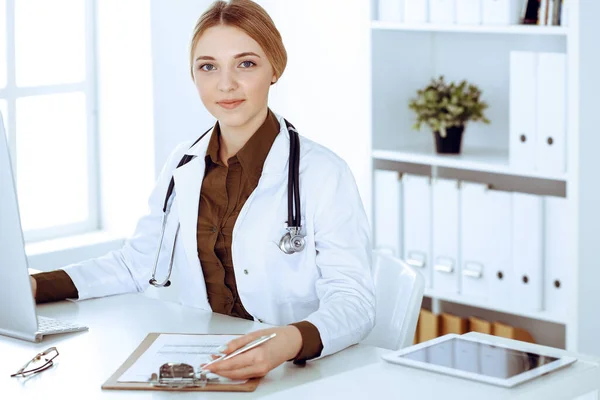 Mujer joven médico en el trabajo en el hospital mirando monitor de escritorio PC. El médico controla los registros de la historia de la medicación y los resultados del examen. Concepto de medicina y salud — Foto de Stock