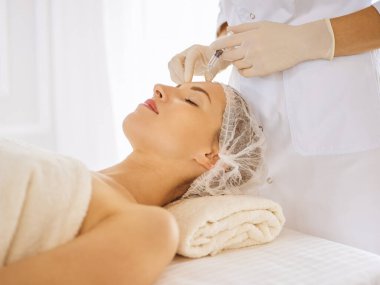 Güzel bir kadın kapalı gözlerle güzellik iğneleri yaptırıyor. Güzellik uzmanı elleri şırıngayla kadın yüzüne güzellik prosedürü uyguluyor.