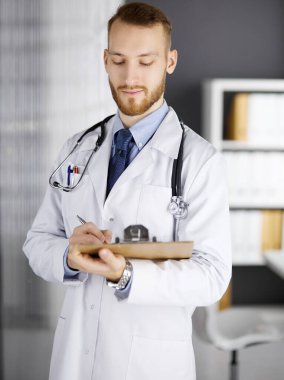 Dost canlısı kızıl sakallı doktor çalışma yerindeki klinikte panoya yazı yazıyor. Hastanede mükemmel bir tıbbi hizmet. Tıp konsepti