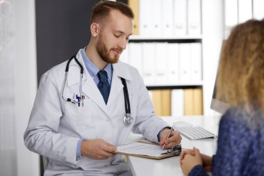 Dost canlısı kızıl sakallı doktor ve hasta kadın güneşli klinikte otururken sağlık muayenesini tartışıyorlar. Tıp konsepti
