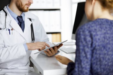 Bilinmeyen kızıl sakallı doktor ve hasta kadın klinikte oturup tablet bilgisayar kullanırken sağlık muayenesini tartışıyorlar. Tıp konsepti